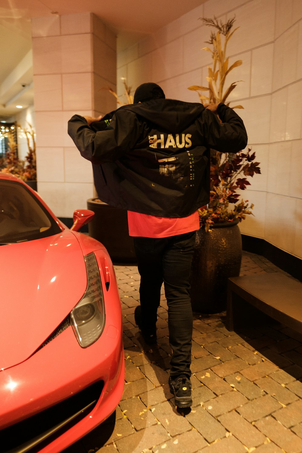 a man in a black jacket walking towards a red sports car