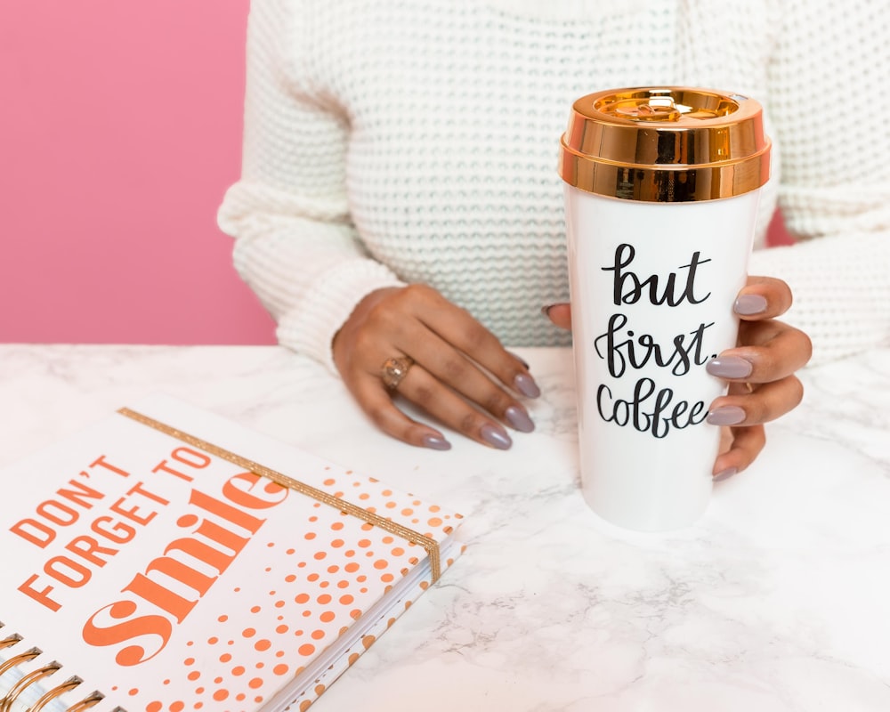 a woman holding a coffee mug next to a book