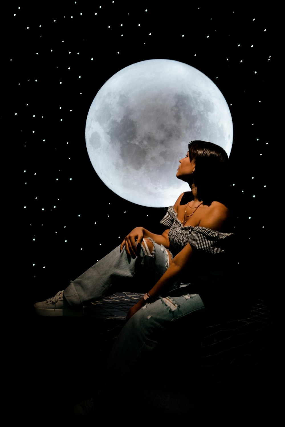 a woman sitting on a bed in front of a full moon