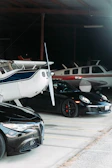 A panoramic view of a private jet hangar lined with exotic cars under soft evening light.