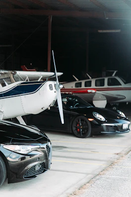 A panoramic view of a private jet hangar lined with exotic cars under soft evening light.
