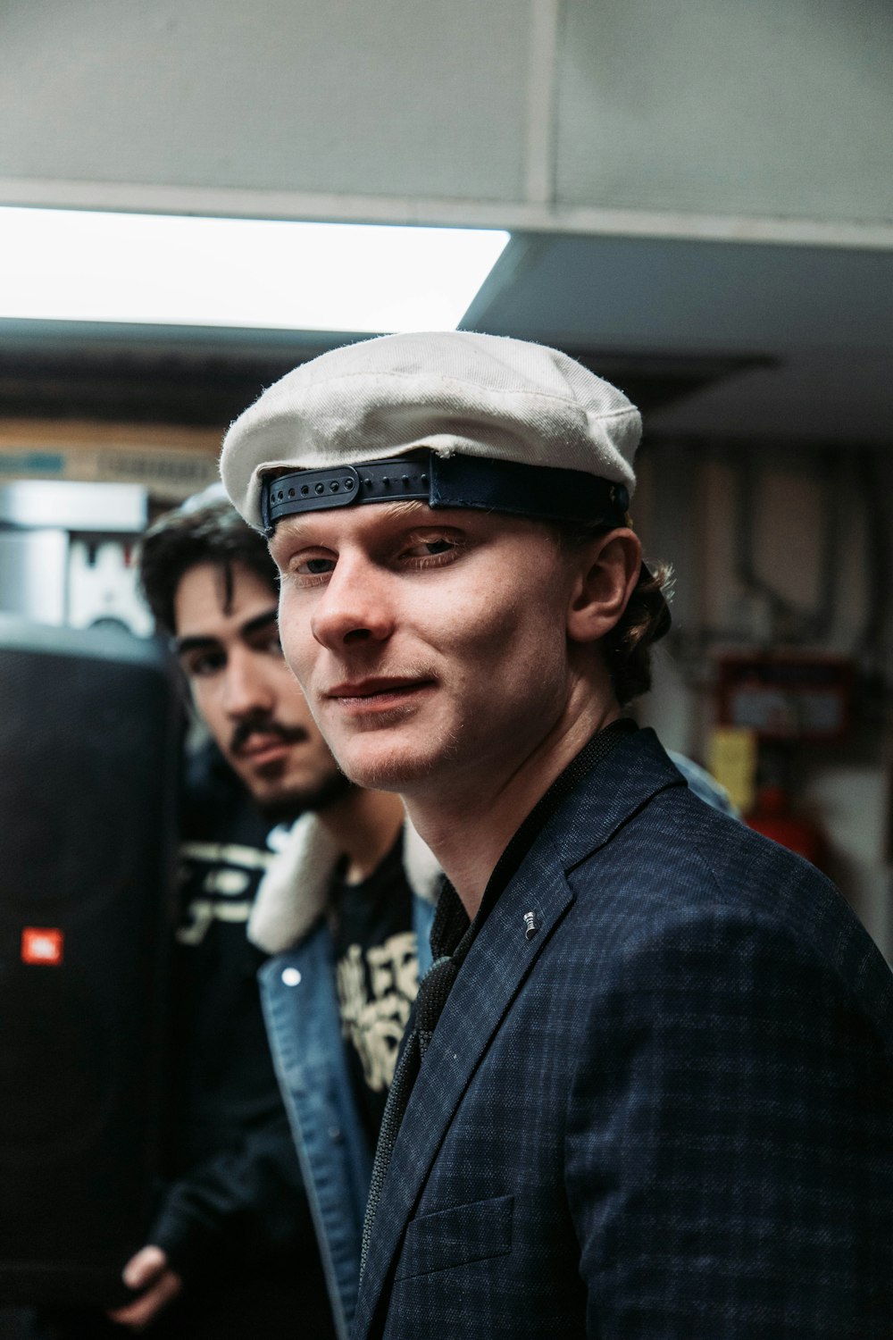 a man wearing a hat and jacket standing next to another man