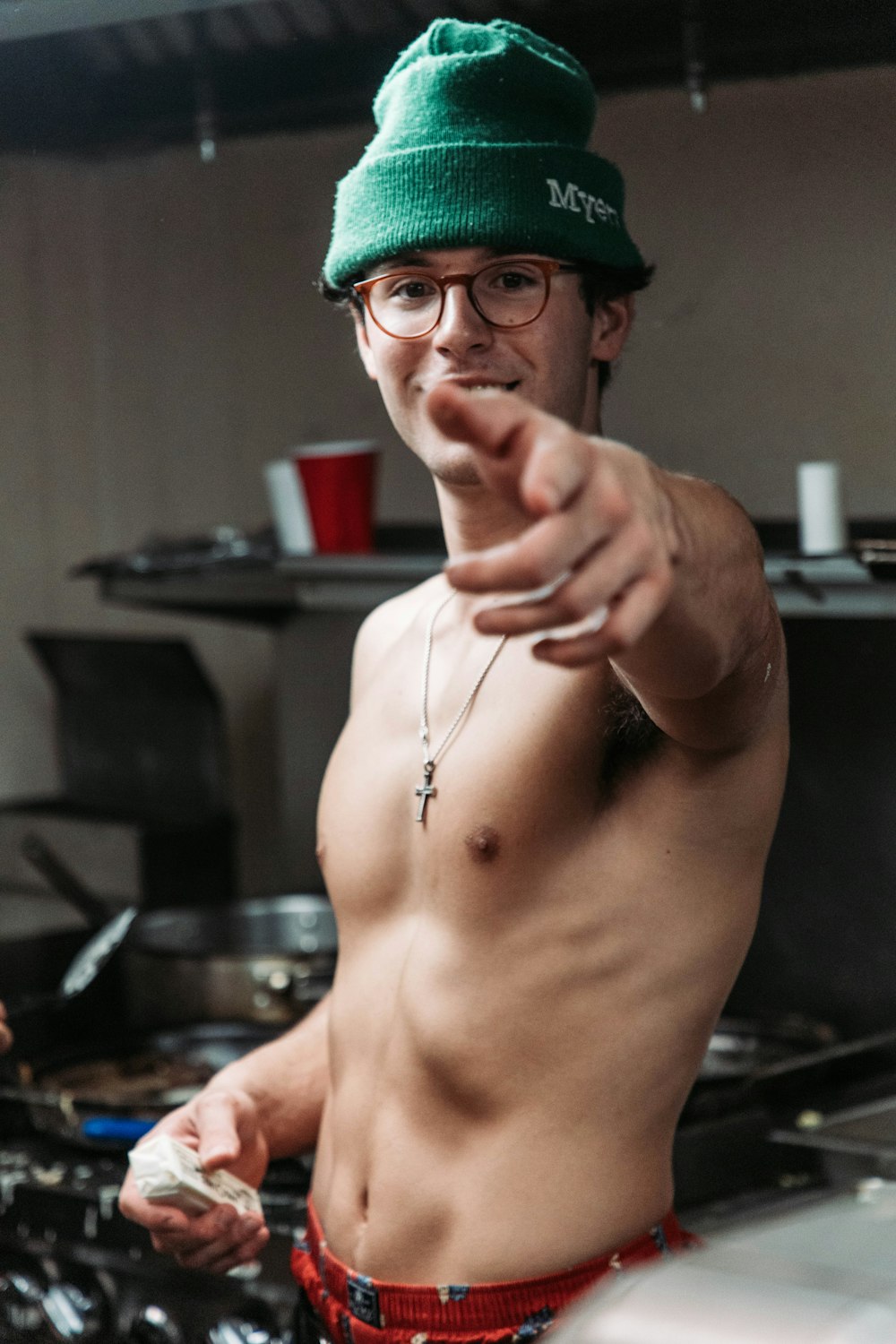 a shirtless man wearing a green hat pointing at the camera