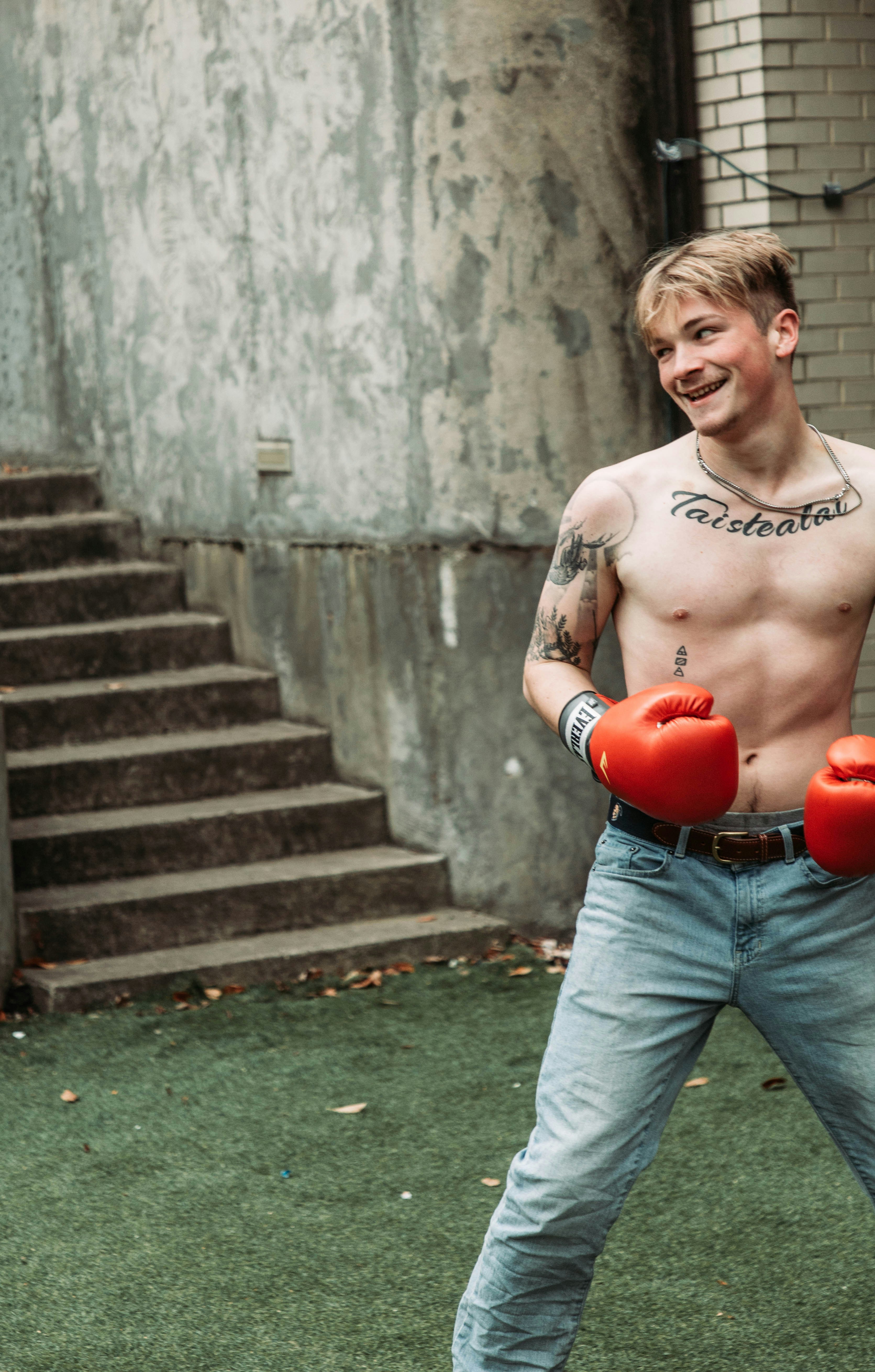 a shirtless man holding two red boxing gloves