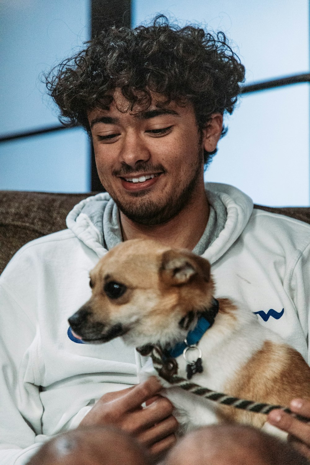 Ein Mann sitzt auf einer Couch und hält einen kleinen Hund in der Hand