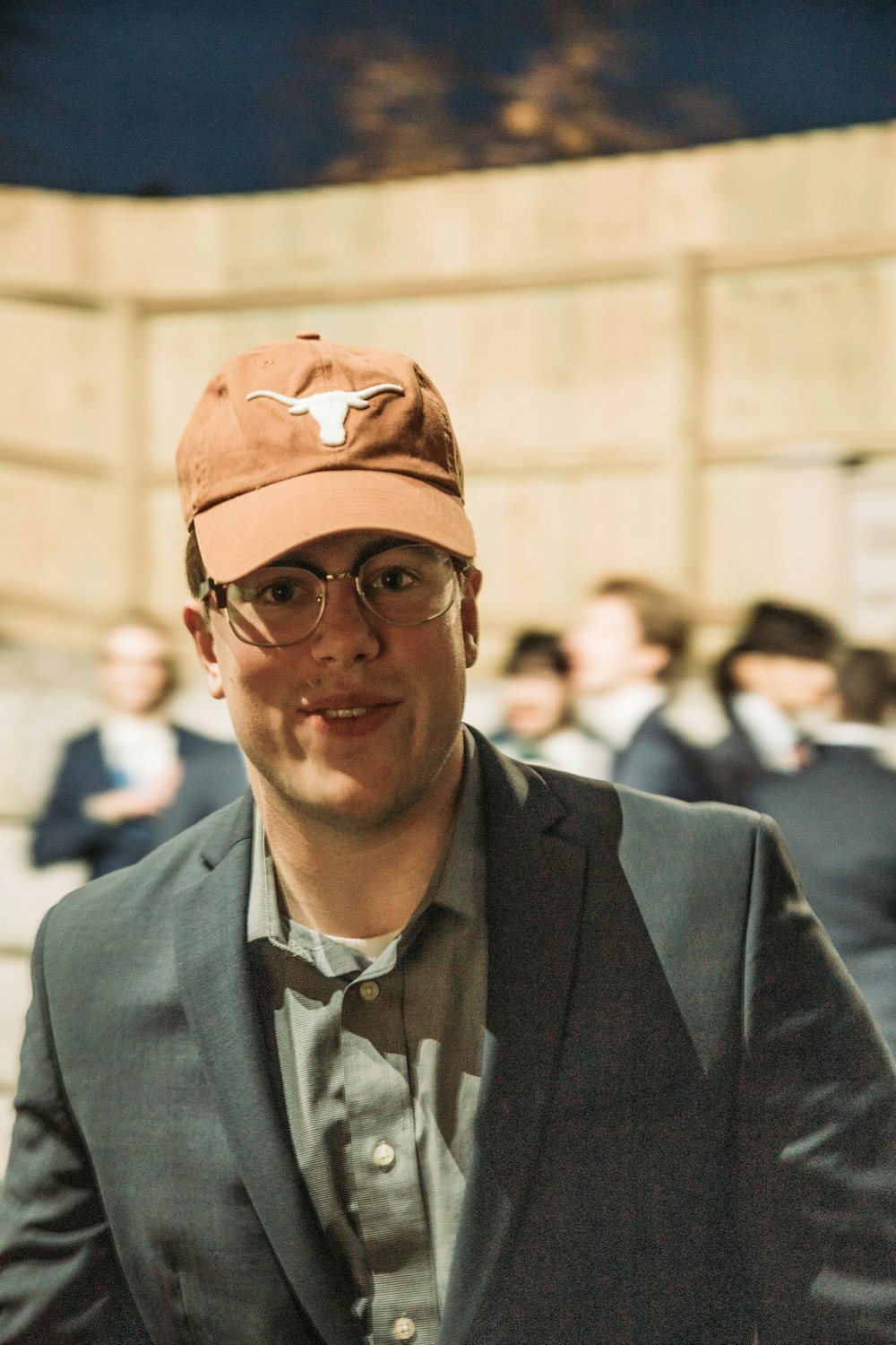 a man wearing a hat and glasses standing in front of a crowd