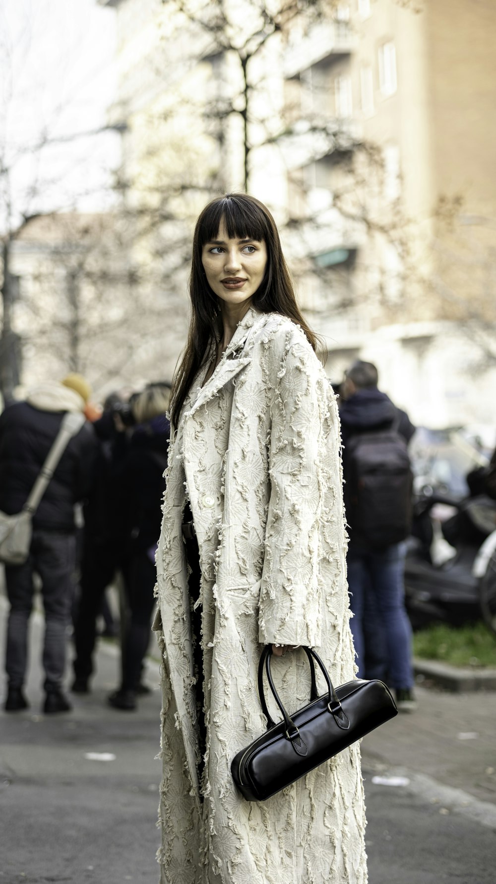 a woman in a white coat is holding a black bag