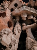 A pile of weathered, rough-textured red and white bricks with visible holes and varying shapes stacked together. The surface of the bricks appears worn and eroded, giving a sense of decay or ruin.
