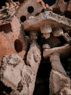 A pile of weathered, rough-textured red and white bricks with visible holes and varying shapes stacked together. The surface of the bricks appears worn and eroded, giving a sense of decay or ruin.