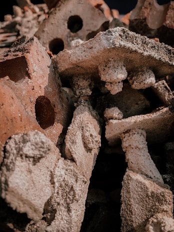 A pile of weathered, rough-textured red and white bricks with visible holes and varying shapes stacked together. The surface of the bricks appears worn and eroded, giving a sense of decay or ruin.