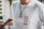 A person is wearing a white t-shirt with the text 'SSUR PLUS' in red and black letters on the front. The individual is also wearing a necklace with a chain and two round pendants. The background appears to have a railing and an out-of-focus cityscape or buildings.