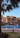 A luxurious outdoor setting featuring a swimming pool surrounded by palm trees and a large, elegant building in the background. The building has an orange facade with arched windows and balconies. Patio furniture is arranged around the poolside, providing a relaxing atmosphere.