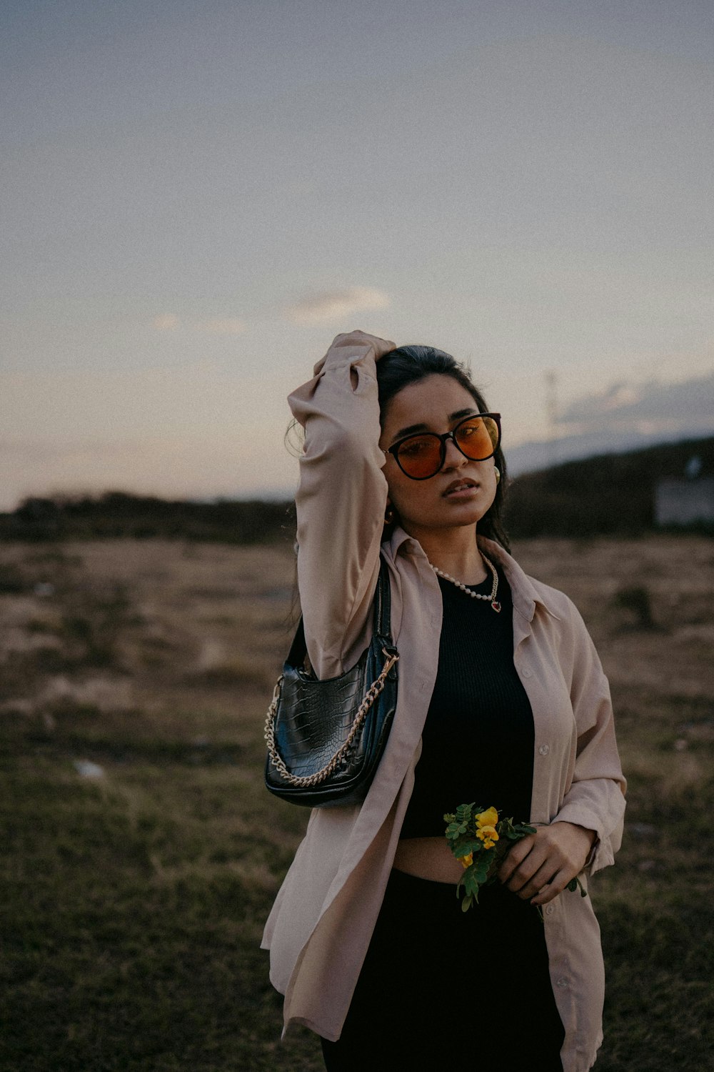 a woman in sunglasses and a jacket holding a flower