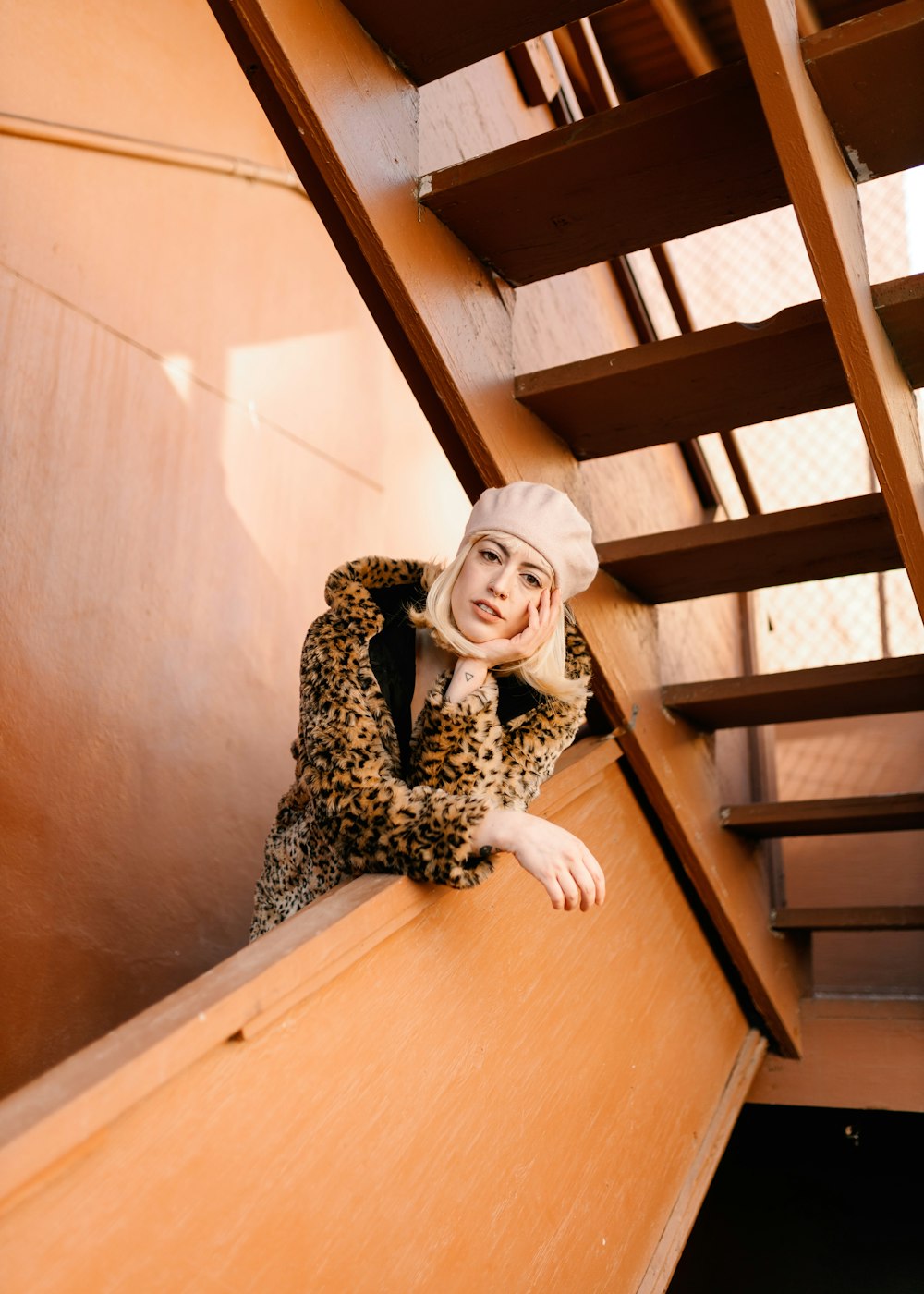 a woman in a leopard print coat leaning on a wooden staircase