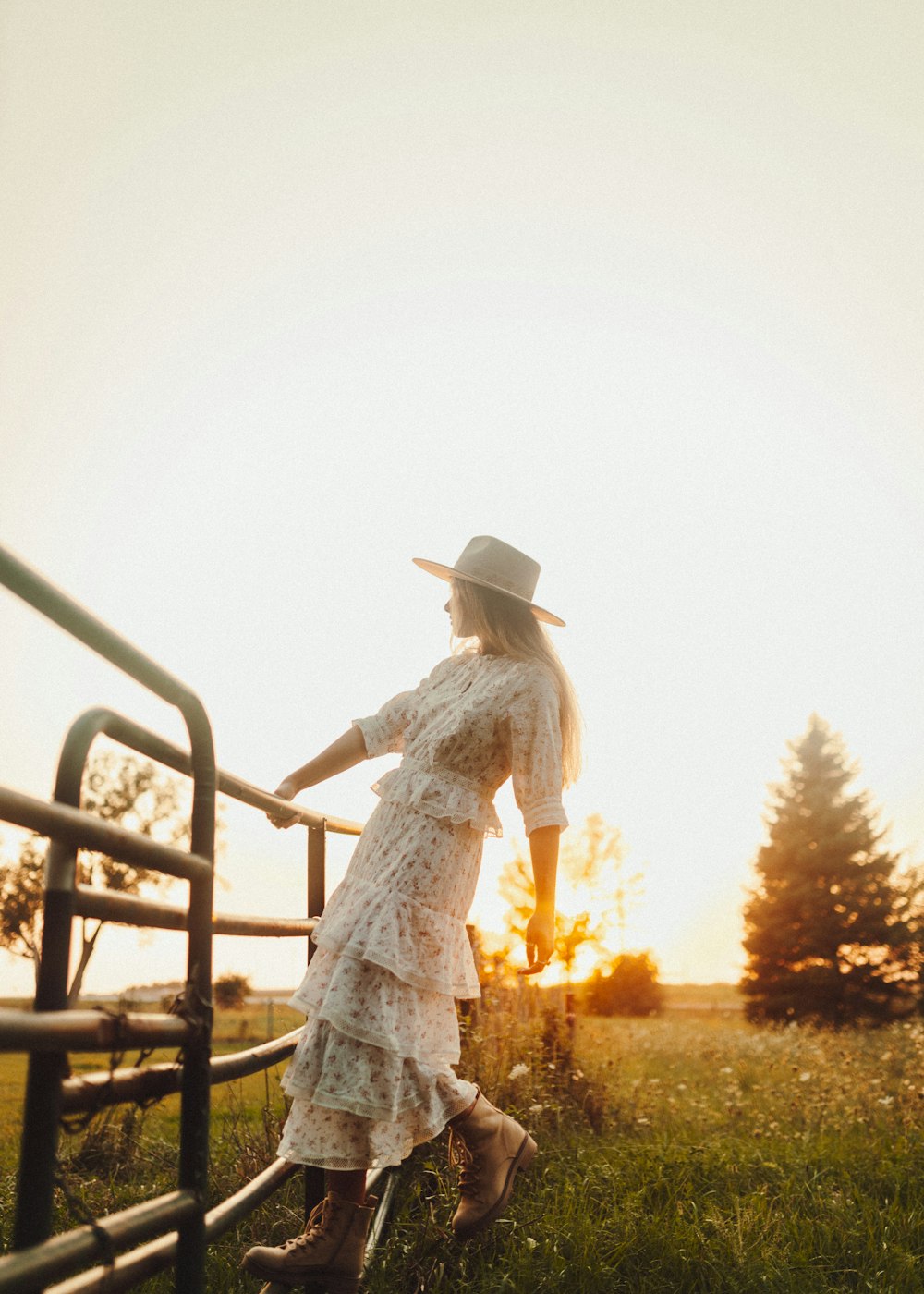 a woman in a dress and cowboy hat leaning on a fence