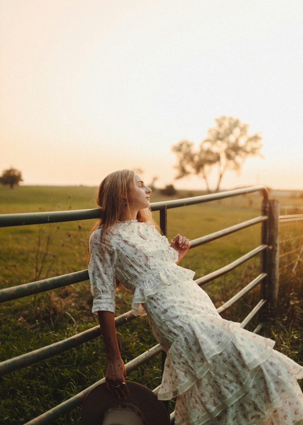a woman in a dress leaning on a fence