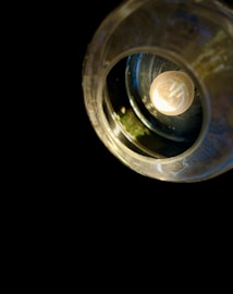 A close-up view of a lit incandescent light bulb surrounded by a metallic or glass fixture, creating a warm glow. The background is entirely dark, emphasizing the bulb's light.