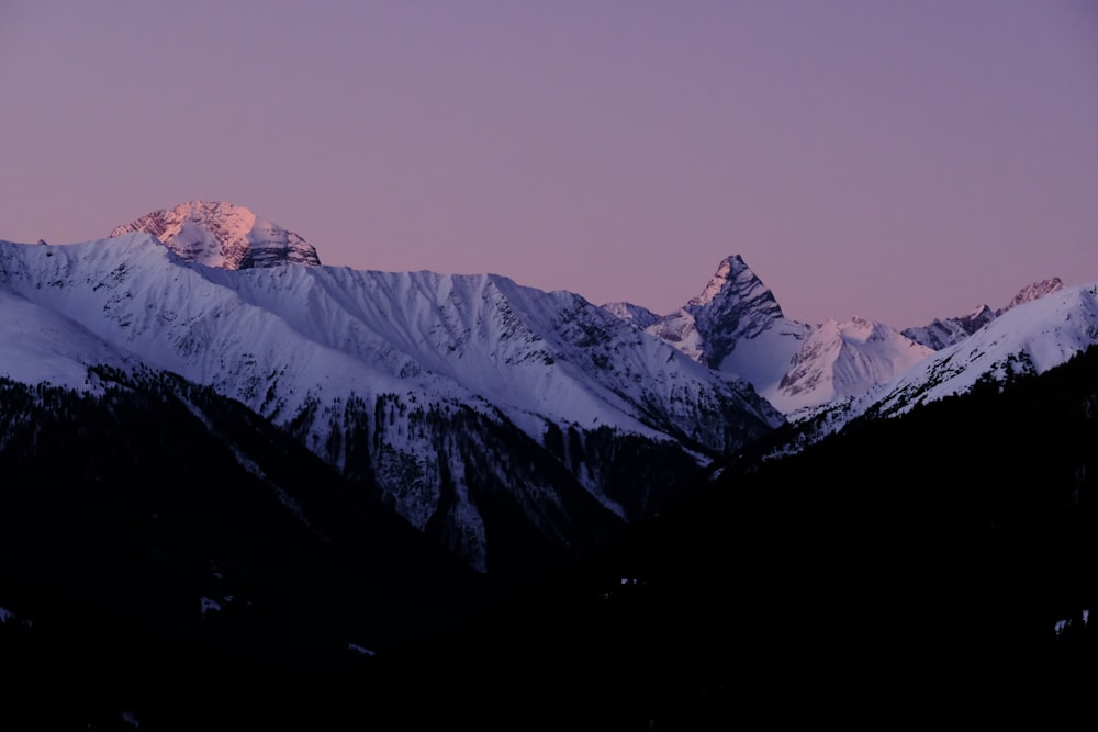 a snow covered mountain range with a purple sky