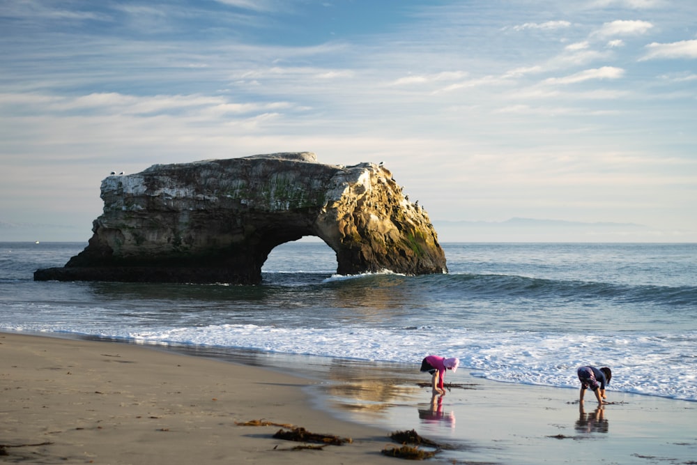 a couple of people standing on top of a sandy beach