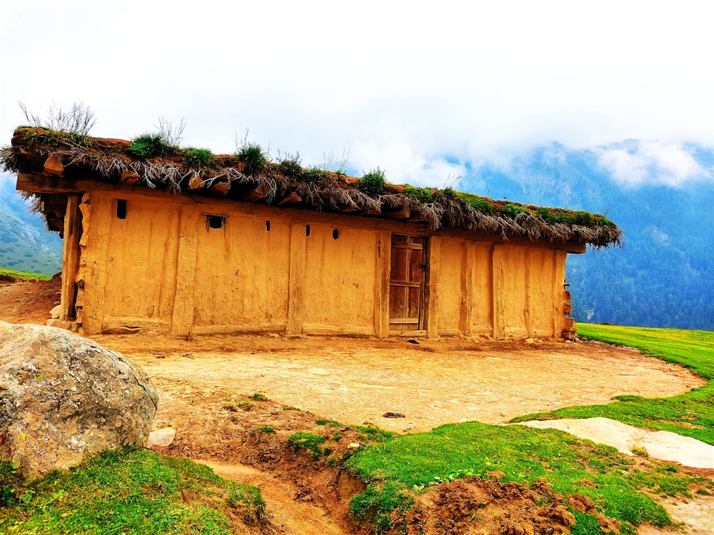 a small building with a grass roof and a rock