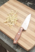 A sleek stainless steel knife resting beside a chopping board with freshly chopped ingredients.