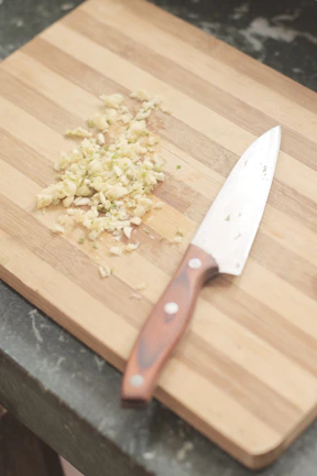 Close-up of a sleek stainless steel garlic press resting on a wooden cutting board.