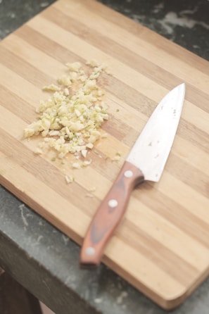 A minimalist wooden cutting board with a sharp chef’s knife resting on it.