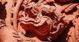 A close-up of an intricately carved dragon or mythical creature in what appears to be terracotta or a similar material. The detailed craftsmanship highlights swirling patterns and sculptural elements, showcasing both the creature's scales and ornate features.