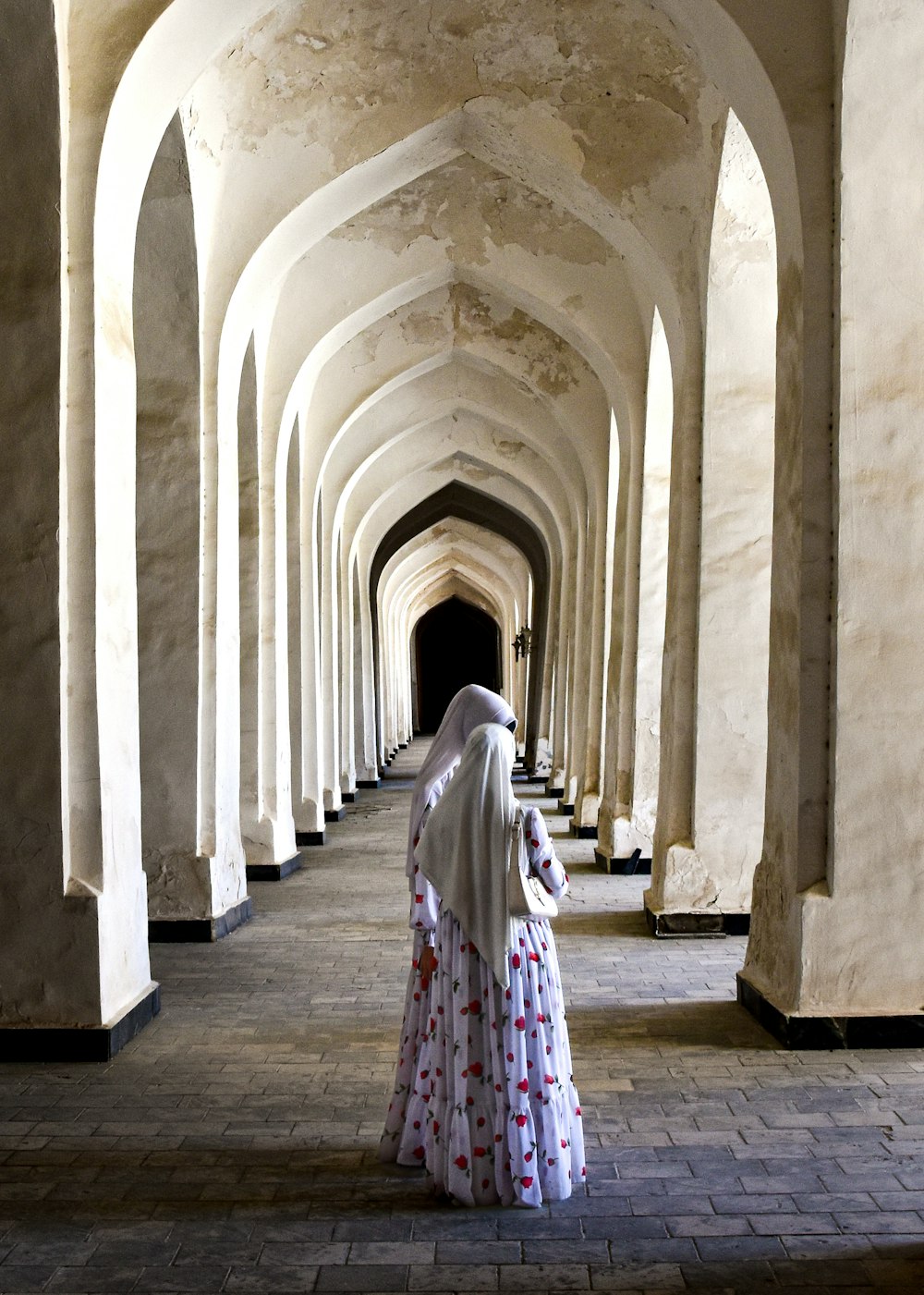 a woman in a white dress is walking down a long hallway