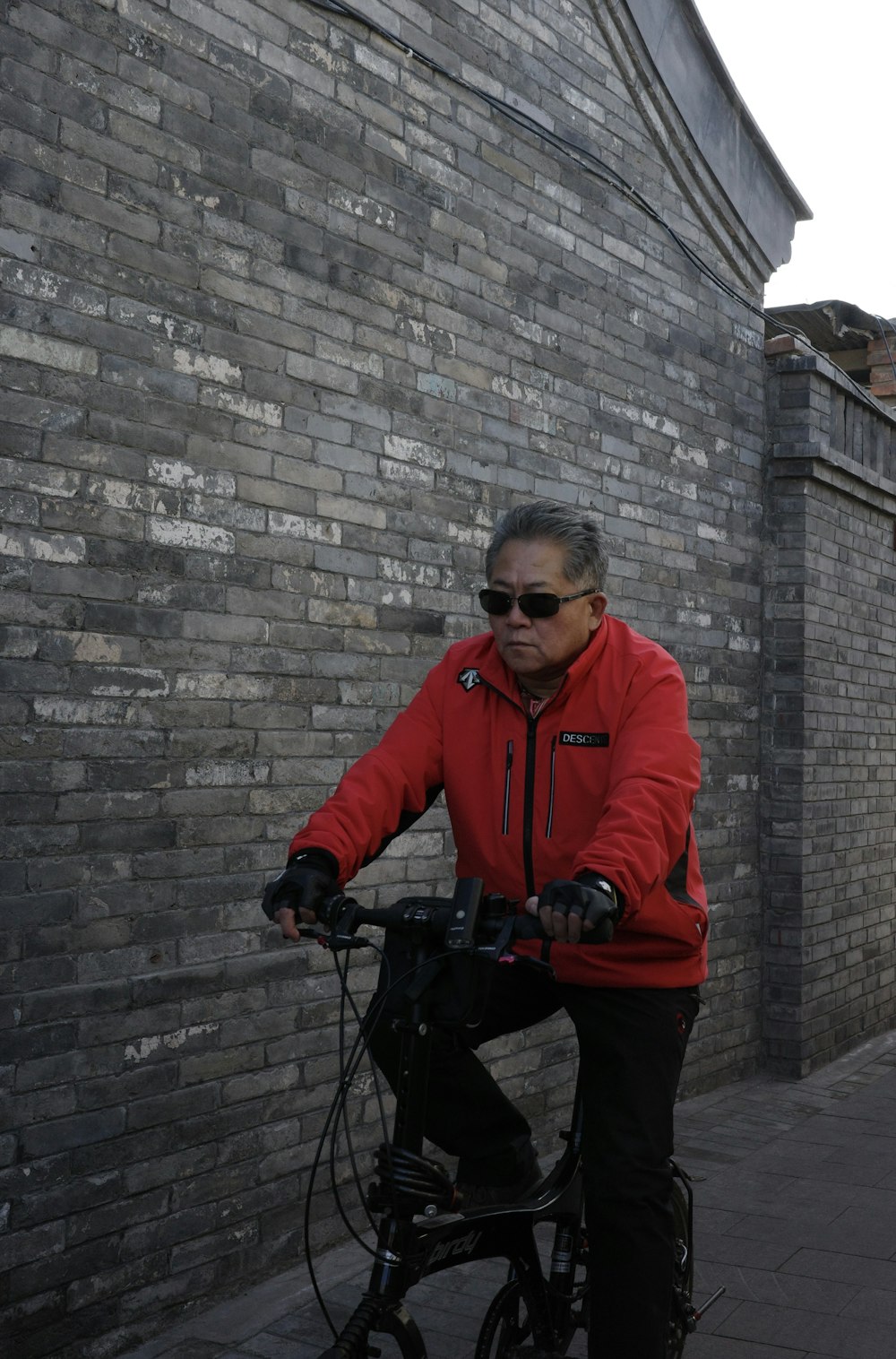 a man riding a bike down a street next to a brick wall