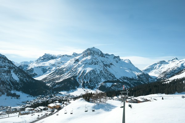 A ski slope and a lift tower below a ring of snow-covered peaks