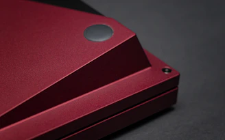 A sleek black and red e-reader glowing on a dark background with sharp-edged geometric shadows.