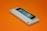 A gaming console cartridge with a predominantly white casing lies on an orange background. The cartridge includes a black and blue label area, with a small red circular detail in the center. A sticker featuring digital art is placed on the label area.