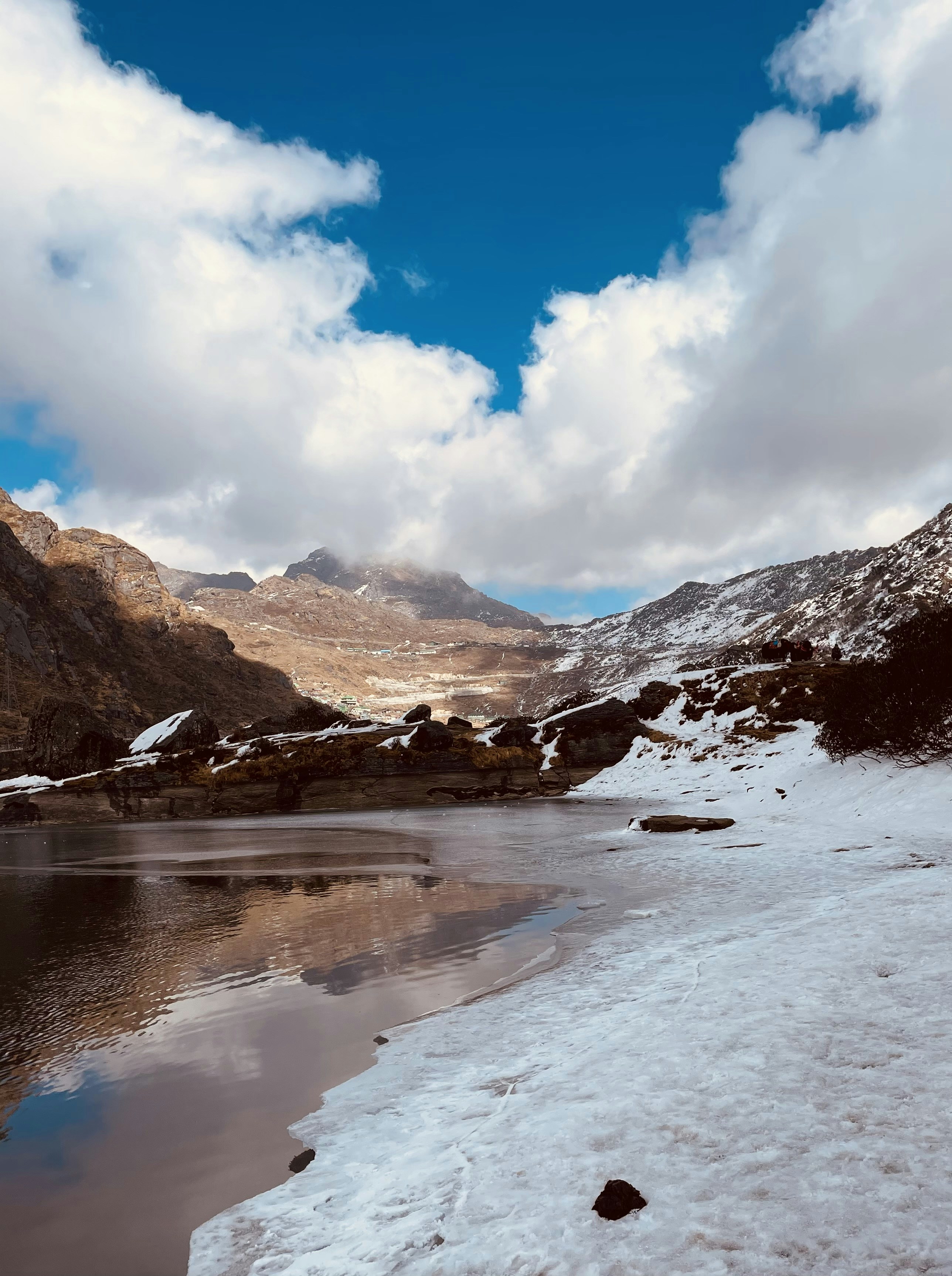 a lake surrounded by snow covered mountains under a cloudy sky