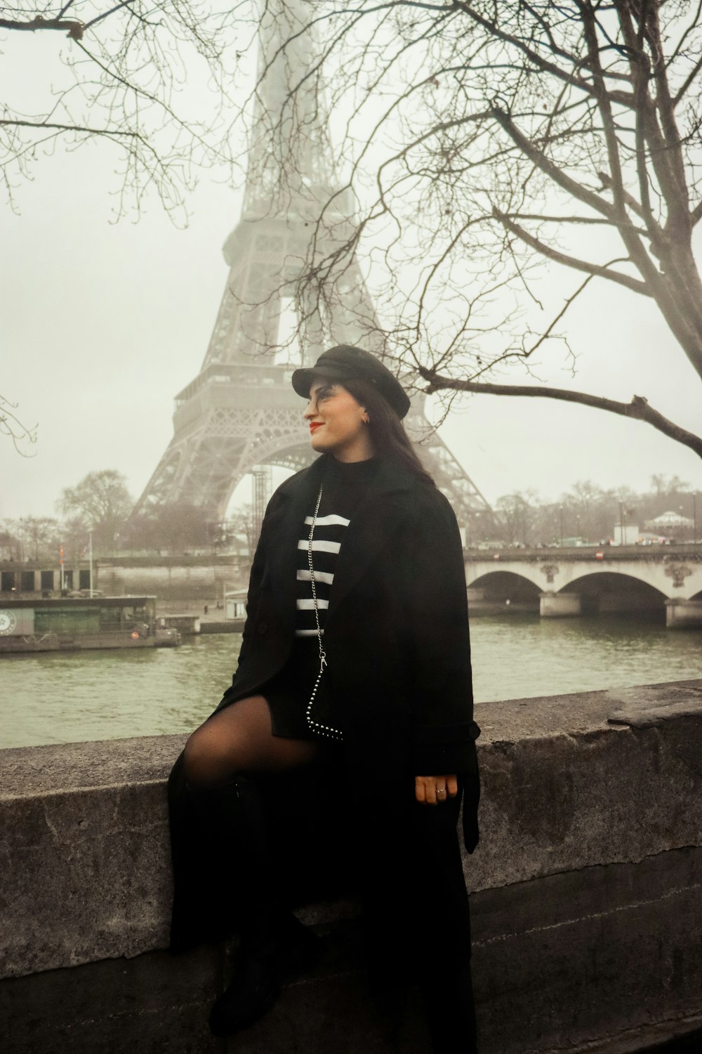 a woman sitting on a ledge in front of the eiffel tower