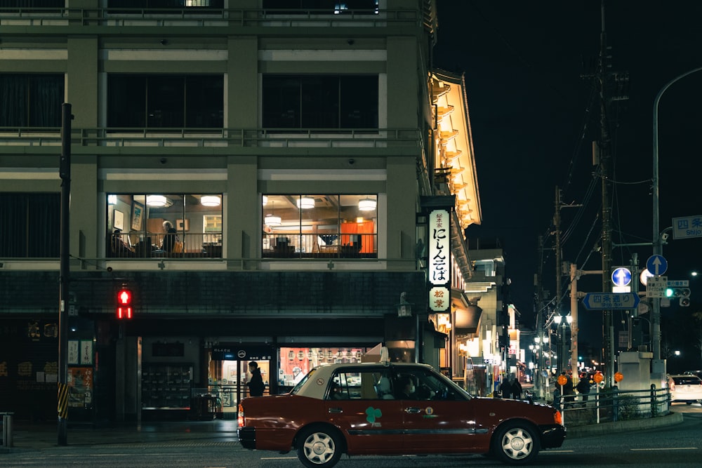 a red car driving down a street at night