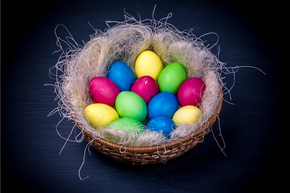 a basket filled with colored eggs on top of a table