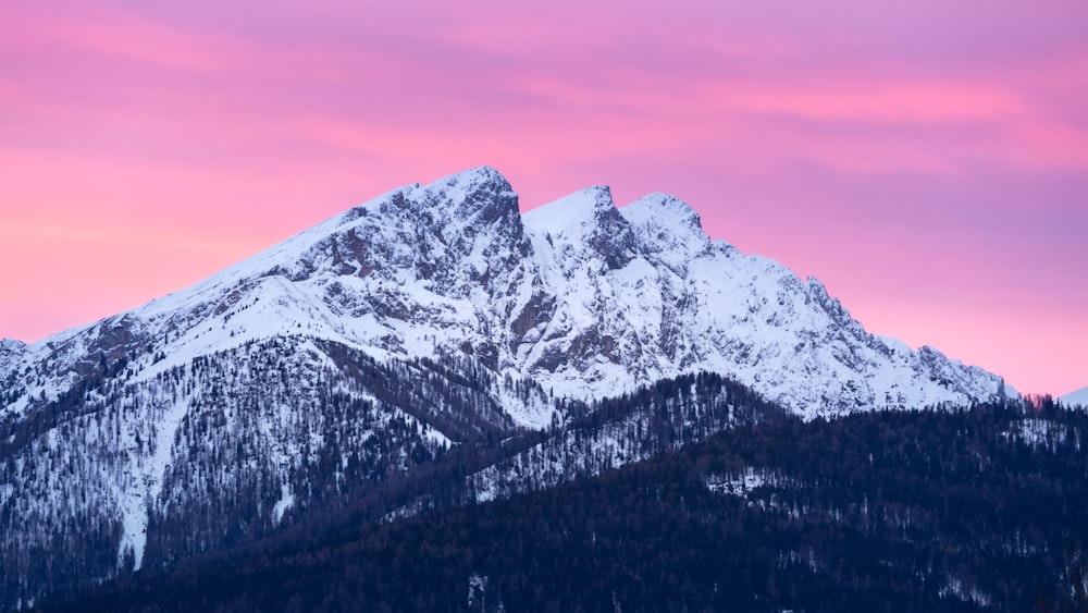 a mountain covered in snow under a pink sky