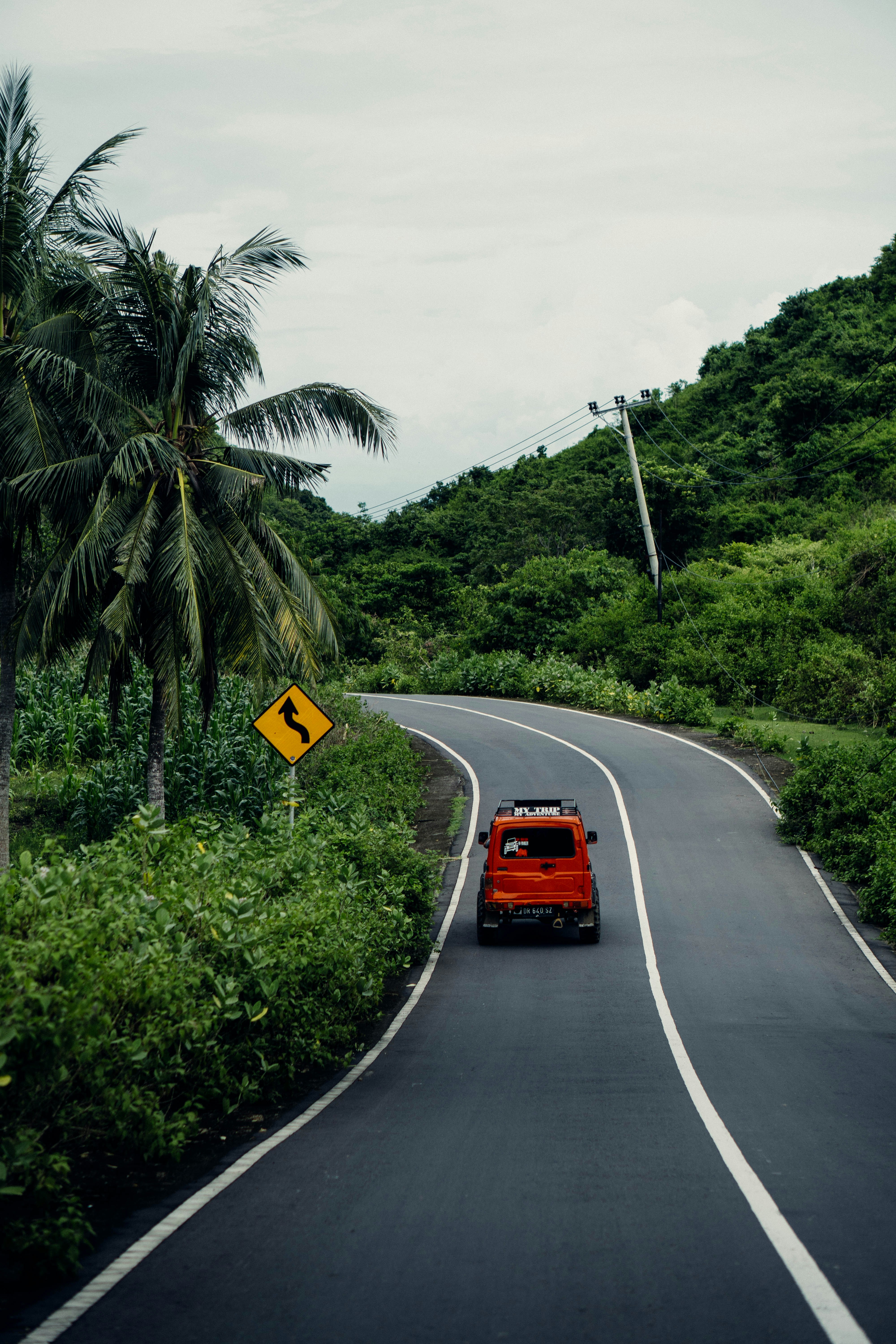 a red car driving down a road next to a lush green hillside