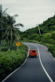 A vibrant red SUV driving through a green tropical forest road.