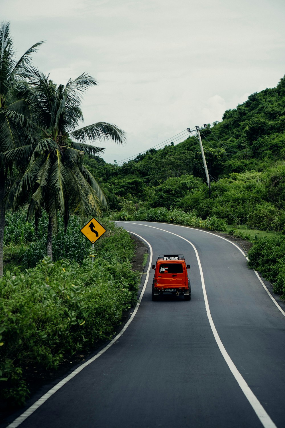 a red car driving down a road next to a lush green hillside