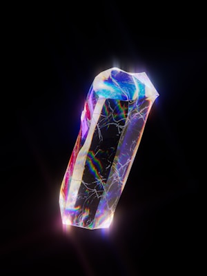 A luminous crystal with a prismatic surface displays a spectrum of colors including blues, purples, and reds, set against a deep black background. The crystal is intricately detailed, with visible cracks and a shiny, iridescent glow.