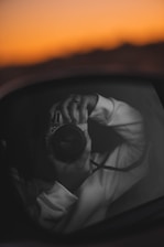A close-up of hands holding a camera, capturing a classic car at sunset.