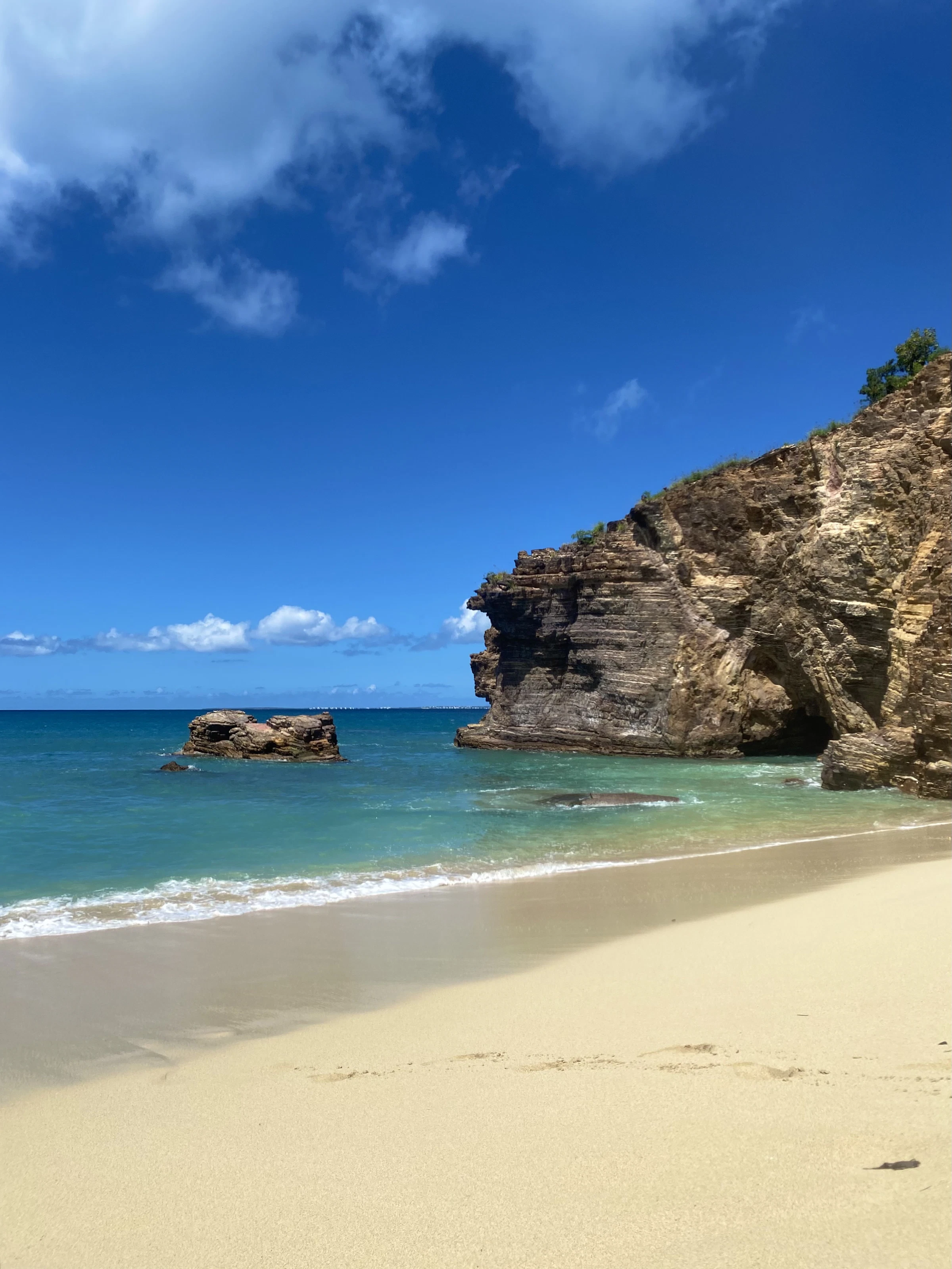 Soft sand and calm turquoise water at Baie Rouge, St. Martin, with rocky headlands under a clear blue sky.