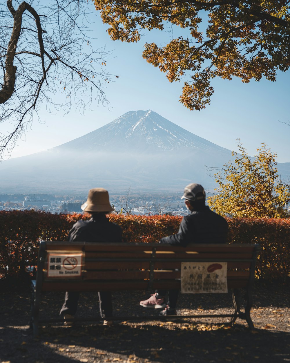 two people sitting on a bench in front of a mountain