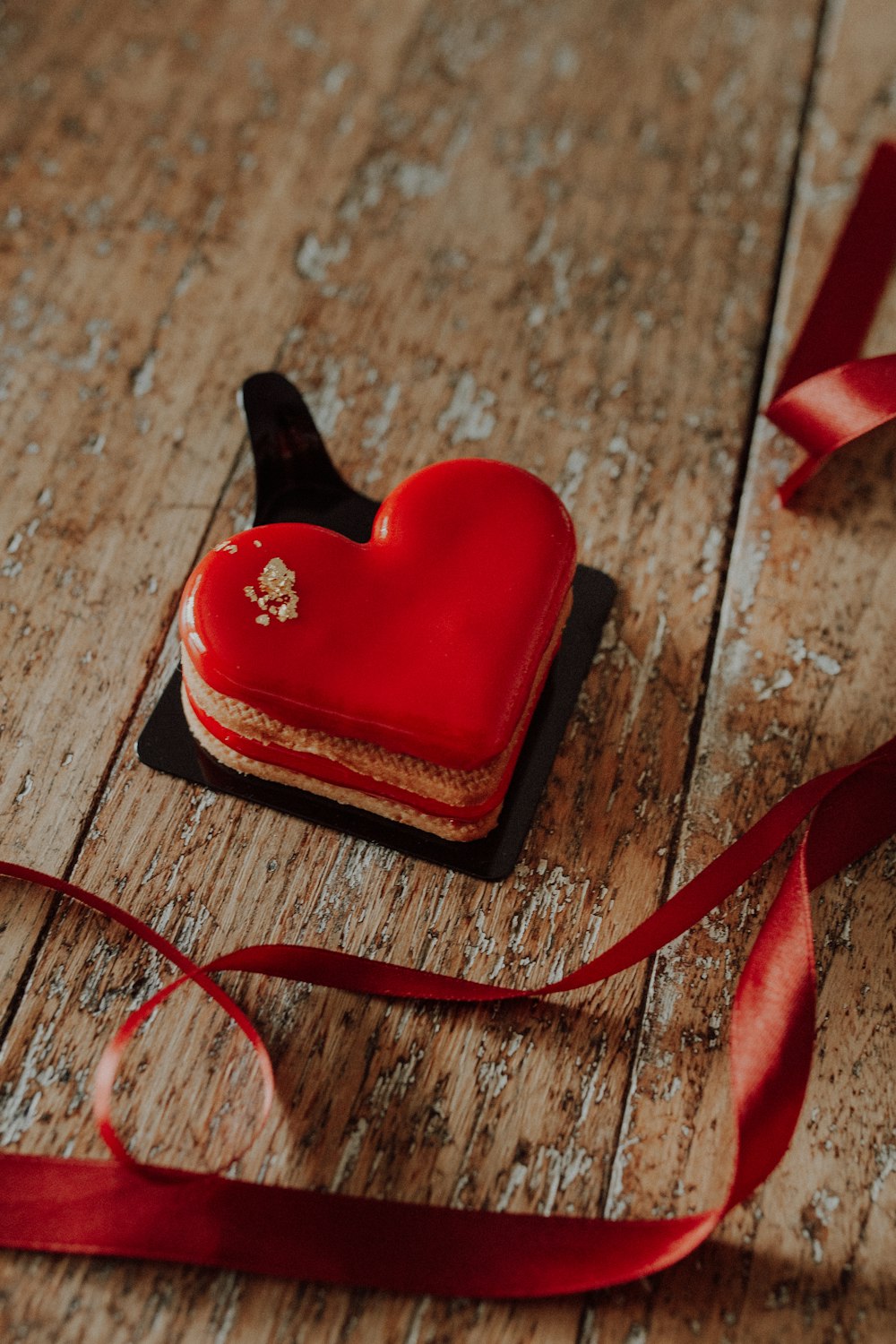 a red heart shaped cookie sitting on top of a wooden table