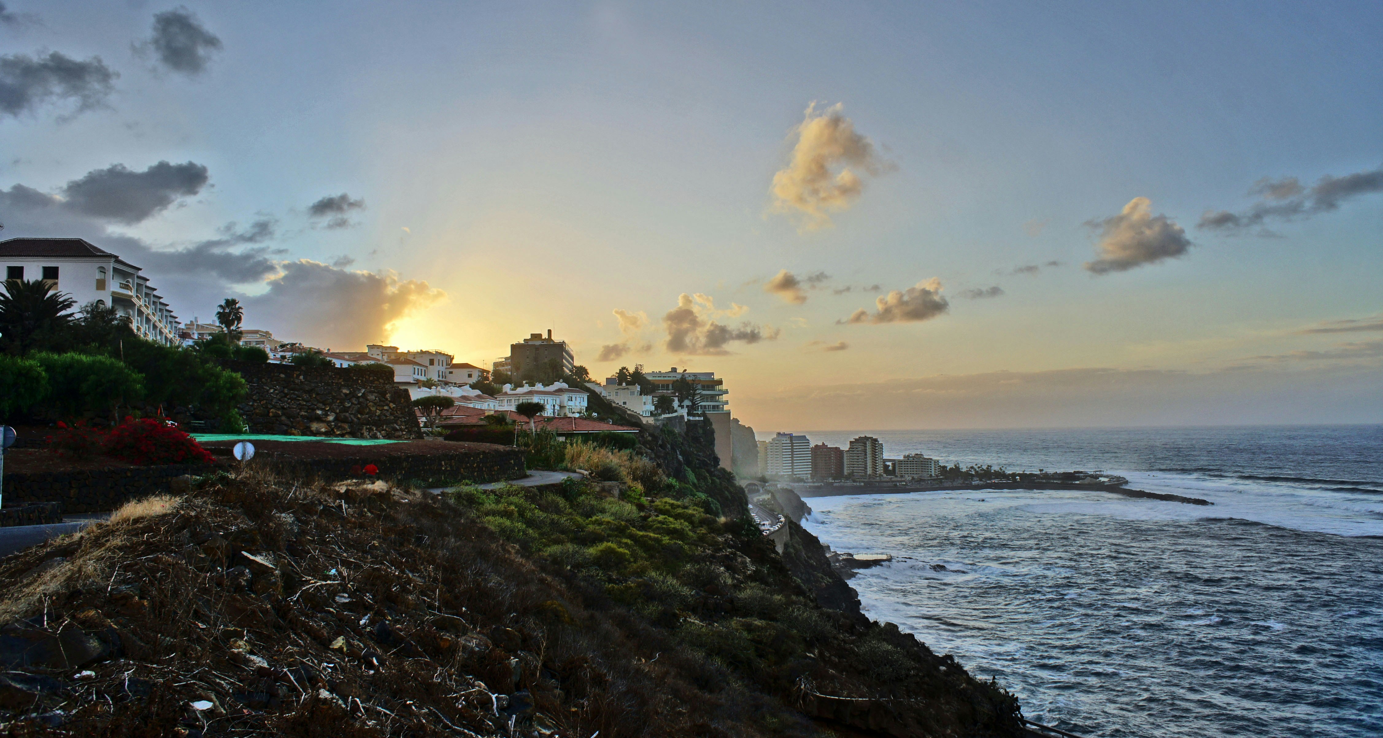 the sun is setting over the ocean and houses on the cliff