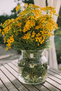 A clear glass vase holding a vibrant bouquet of fresh wildflowers on a sunlit wooden table.