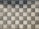 A pattern of square pavers arranged in a checkered layout with alternating light and dark shades of gray. The surface texture of each paver is rough and pebble-like.