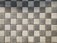 A pattern of square pavers arranged in a checkered layout with alternating light and dark shades of gray. The surface texture of each paver is rough and pebble-like.